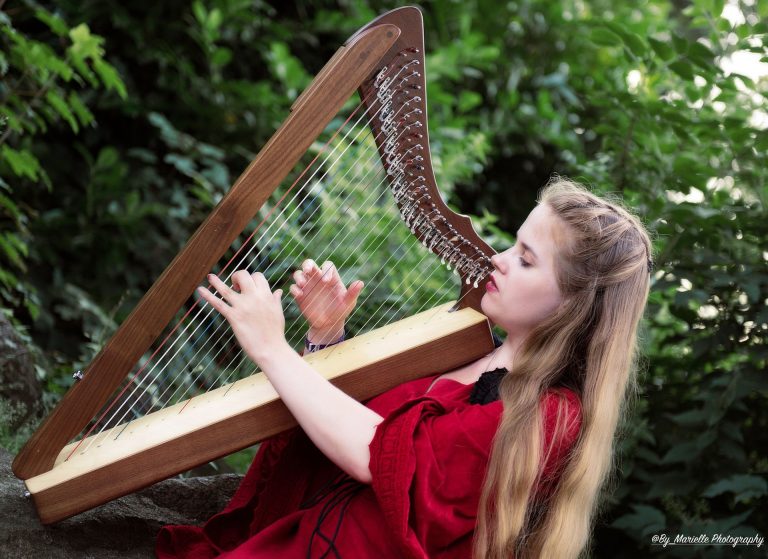 Cathinca in rode jurk speelt harp